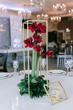 red flowers are in a gold geometric vase on a white table cloth with greenery