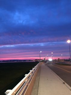 the sun is setting over an empty road and some lights are shining in the distance