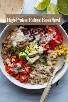 a white bowl filled with rice, beans and vegetables next to limes on the side