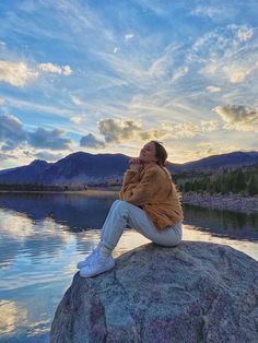 a woman sitting on top of a rock next to a lake