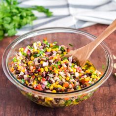 a wooden spoon in a glass bowl filled with black beans, corn and cilantro