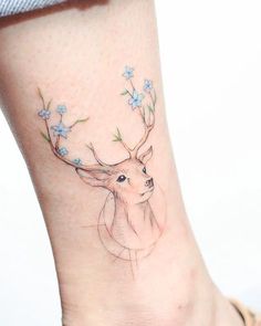 a small deer tattoo on the ankle with blue flowers around its antelope's head