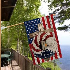 an american flag hanging from a porch with the eagle and cross painted on it's side