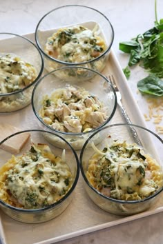 four glass bowls filled with food on top of a white tray next to spinach leaves