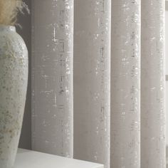 a white vase sitting on top of a table next to a window covered in curtains