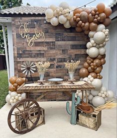 an outdoor table with balloons and decorations on the wall, along with a wagon filled with flowers