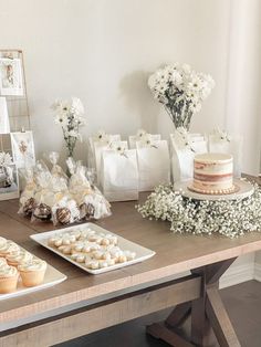 a table topped with cakes and cupcakes on top of a wooden table covered in white flowers