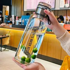 a person holding up a large glass bottle with limes in it and water inside