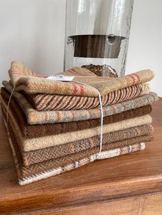 a stack of towels sitting on top of a wooden table next to a glass vase