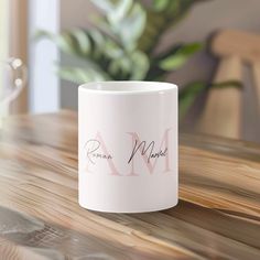 a white coffee mug sitting on top of a wooden table next to a potted plant