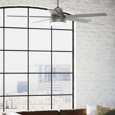 a living room with a couch and ceiling fan in front of a large window that overlooks the city