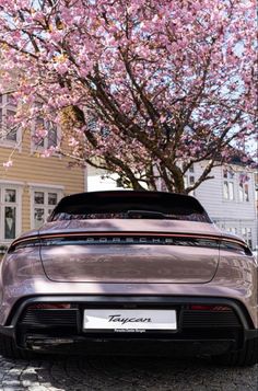 the back end of a silver sports car parked in front of a tree with pink flowers