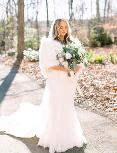 a woman in a white dress and fur coat holding a bouquet on her wedding day