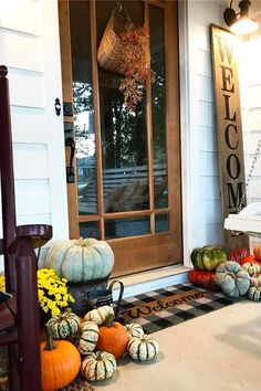 pumpkins and gourds are sitting on the front porch with welcome sign in the background