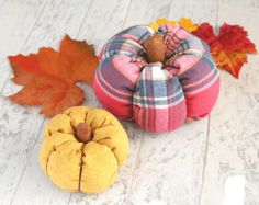 two small pumpkins sitting next to each other on a white wooden floor with autumn leaves