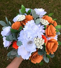 a bridal bouquet with orange, white and grey flowers is held in someone's hand