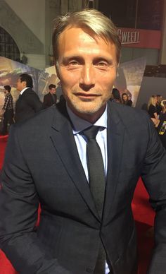 a man in a suit and tie posing for a photo on the red carpet at an event