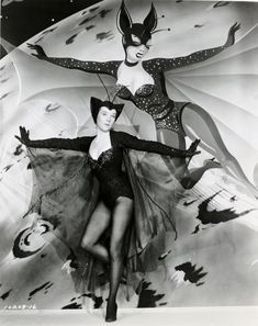 an old photo of two women dressed in catsuits and costumes, posing for the camera