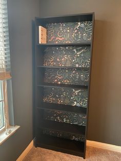 a bookcase with many different designs on it in the corner of a room next to a window