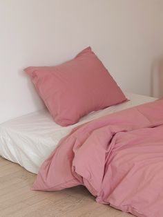 a bed with pink sheets and pillows on top of it next to a white wall