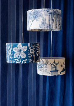 three lamps hanging from the ceiling in front of a blue curtain with trees and flowers on them