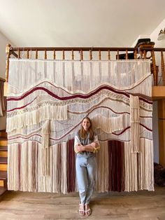 a woman is standing in front of a wall hanging with fringes and beads on it