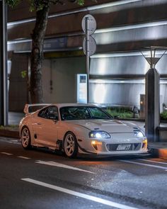 a white sports car parked on the side of the road at night time with its lights on