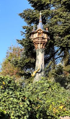 a tall tower with a clock on it's side surrounded by trees and bushes