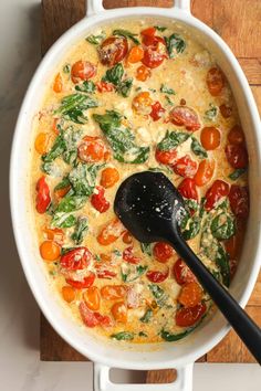 a pot filled with tomatoes and spinach on top of a wooden cutting board