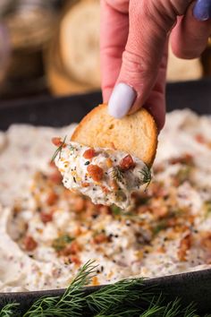 a hand dipping a cracker into a bowl of dip