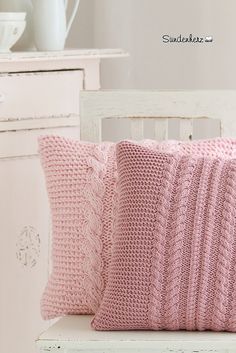 a pink knitted pillow sitting on top of a white chair next to two pillows