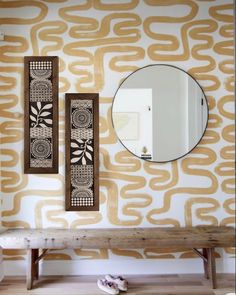 a bench and mirror in front of a wall with an abstract design on it,