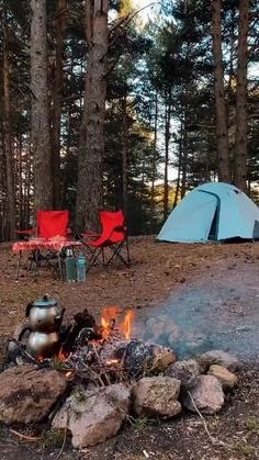 there is a tent in the woods next to a campfire with chairs around it