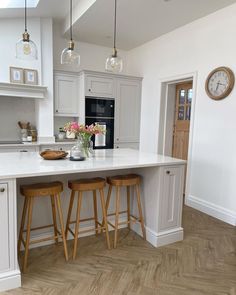 a kitchen with two stools next to an island and clock on the wall above it