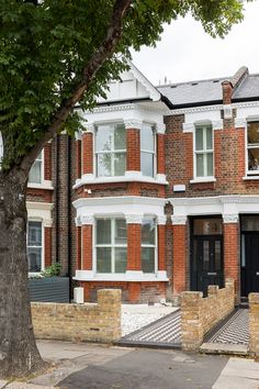 a large red brick house with white trim and shutters on the front door is next to a tree