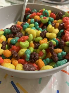 a bowl filled with lots of different colored candy beans next to a spoon on top of a table