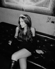 a woman sitting on top of a black couch wearing a tiara and high heels