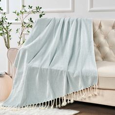 a white couch with a light blue blanket on it and a potted plant in the corner