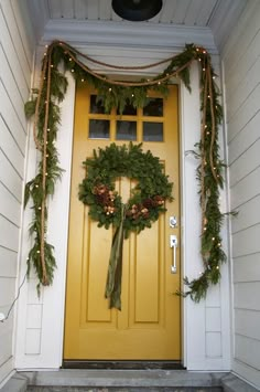 a yellow door decorated with christmas wreaths and lights