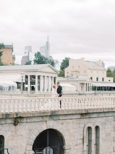 a bride and groom standing on top of a stone bridge in front of a cityscape