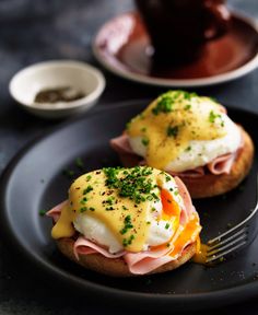 two open faced sandwiches with ham, cheese and hollandaise sauce on a black plate