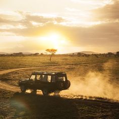 a jeep driving down a dirt road in the middle of a grassy field at sunset