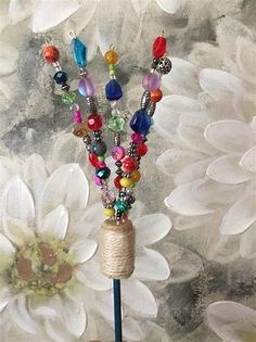 a hand holding a beaded necklace on top of a blue stick with flowers in the background