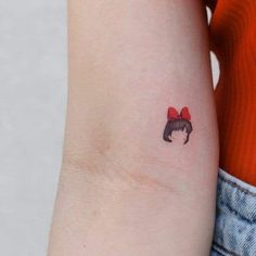 a woman's arm with a small red bow tattoo on the left side of her arm