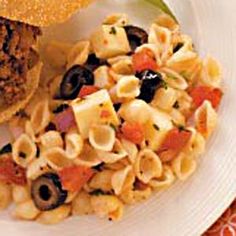 a white plate topped with pasta and meat next to a sandwich on top of a table