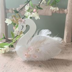 a white swan decoration sitting on top of a wooden table next to flowers and leaves