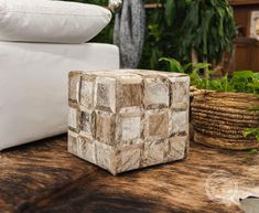 a white couch sitting next to a wooden table with pillows on it and plants in the background