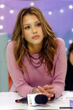 a young woman sitting at a table with her hands folded in front of her face