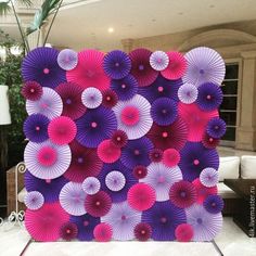 a purple and pink backdrop with paper fans on the wall in front of a couch