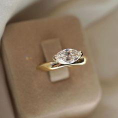 an engagement ring with a pear shaped diamond on it's side in a box